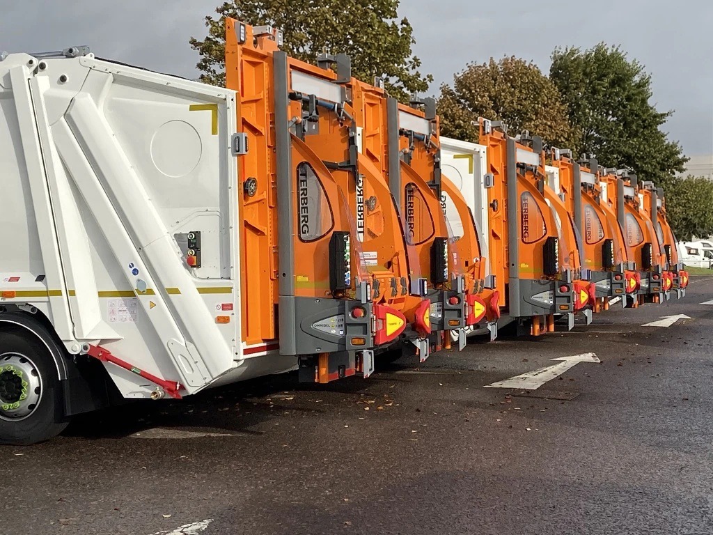 Orange and white refuse collection vehicles lined up outside a depot